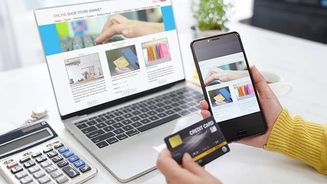 Almost all online activities can contribute to your digital footprint. Image shows somebody holding their phone and credit card up in front of a computer screen with an online shopping window open.